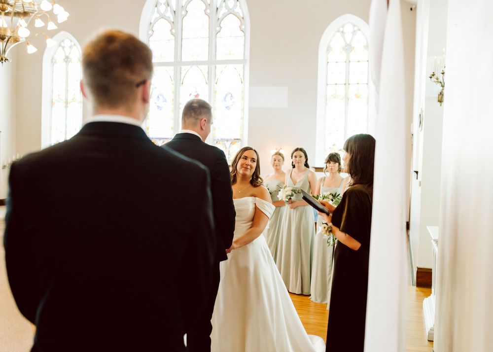 Wedding ceremony in progress inside a bright church with arched windows.