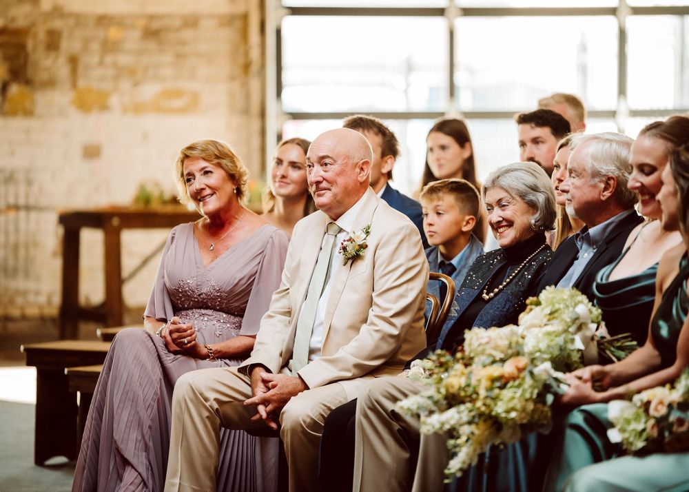 Wedding guests in formal attire seated in rows during an indoor ceremony.