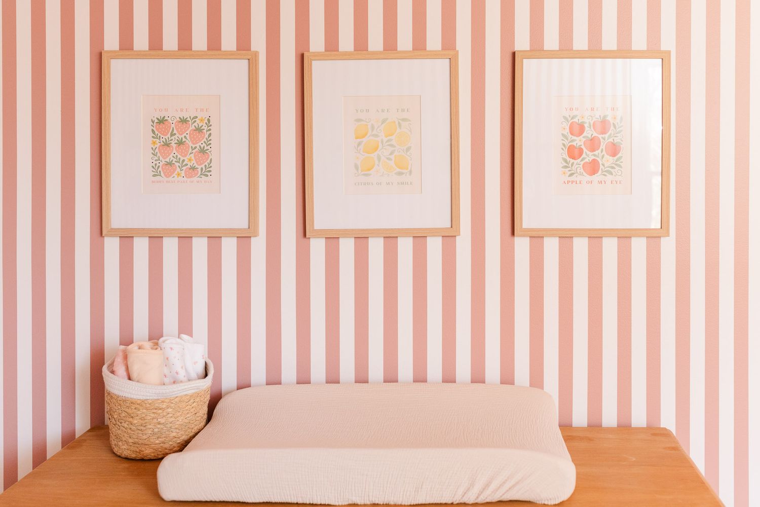 Baby changing table with framed fruit prints hanging on the wall above.