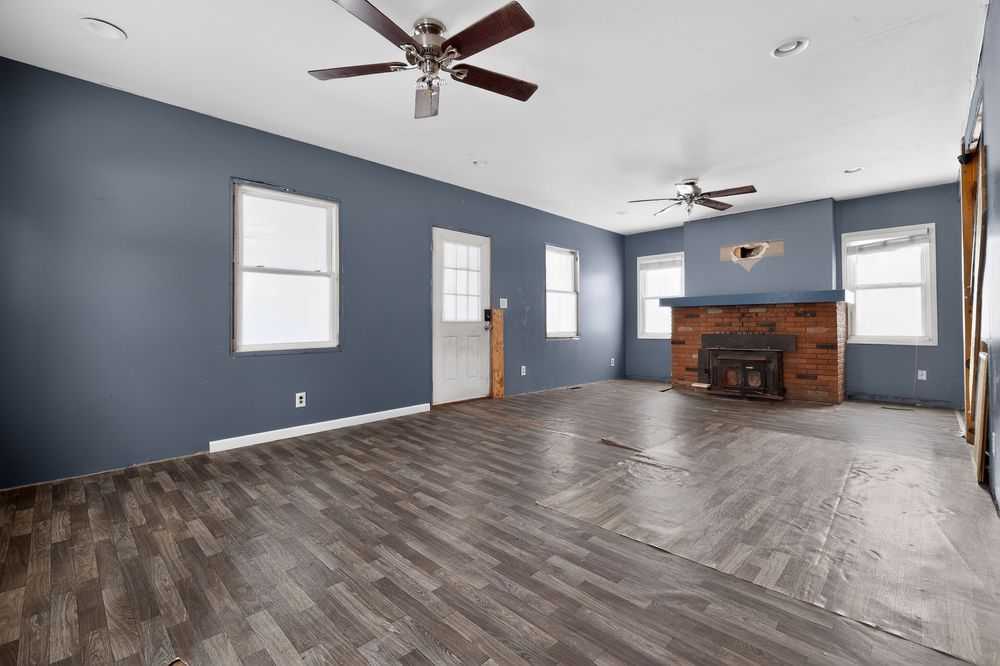 Spacious living room with blue walls, dark hardwood floors, wood-burning fireplace, and dual ceiling fans.