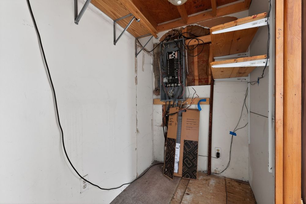Unfinished basement storage space with exposed HVAC unit, wiring, and wooden ceiling beams.