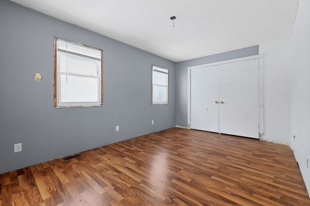 Bright empty bedroom with hardwood floors, two windows, and a white closet door.