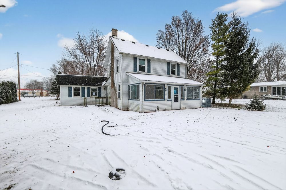 Two-story farmhouse with enclosed front porch surrounded by snow-covered yard in winter.