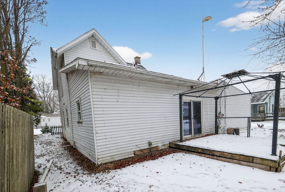 Side view of white two-story home with enclosed porch addition and snow-covered yard.