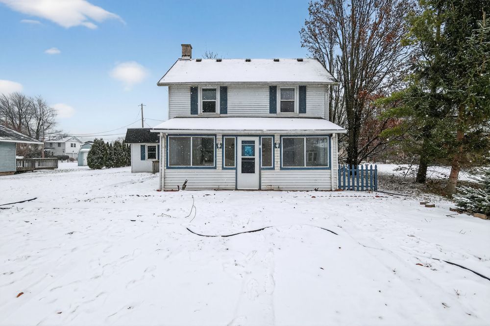 Front view of a two-story white colonial home with screened porch entrance surrounded by fresh snow in winter.