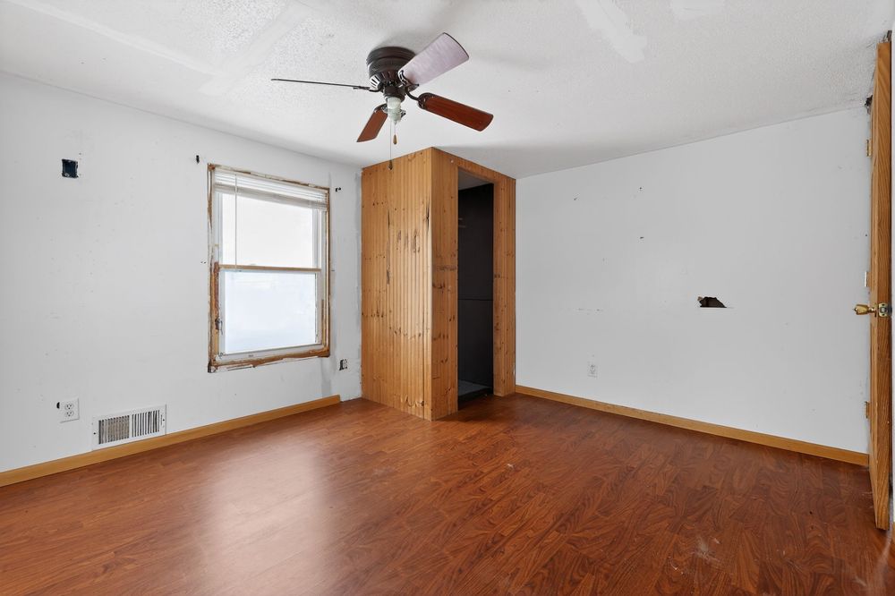 Empty bedroom with hardwood floors, ceiling fan, wood-trimmed closet door, and single window with natural light.