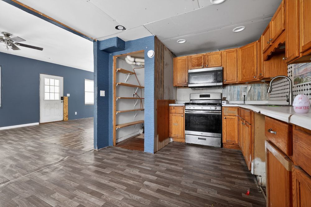 Kitchen with oak cabinets, stainless steel appliances, dark hardwood floors, and open shelving in blue dining area.