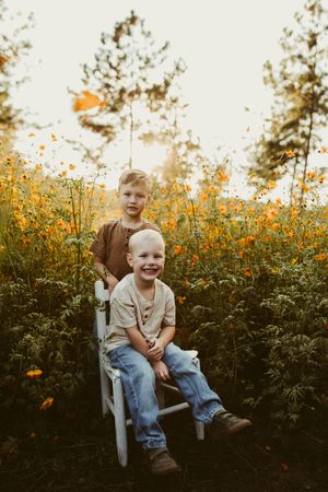 Two young brothers posing in a white wagon surrounded by orange wildflowers at golden hour.