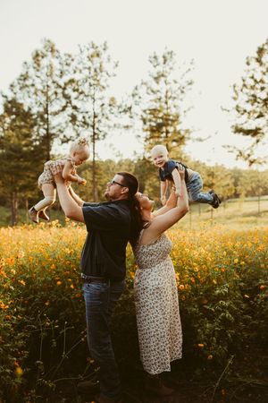 Happy family lifting two babies in a vibrant orange wildflower field at sunset.