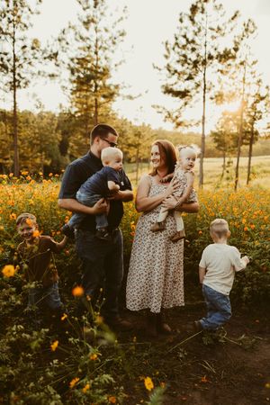Family of five posing together in a golden sunlit field of orange wildflowers at dusk.