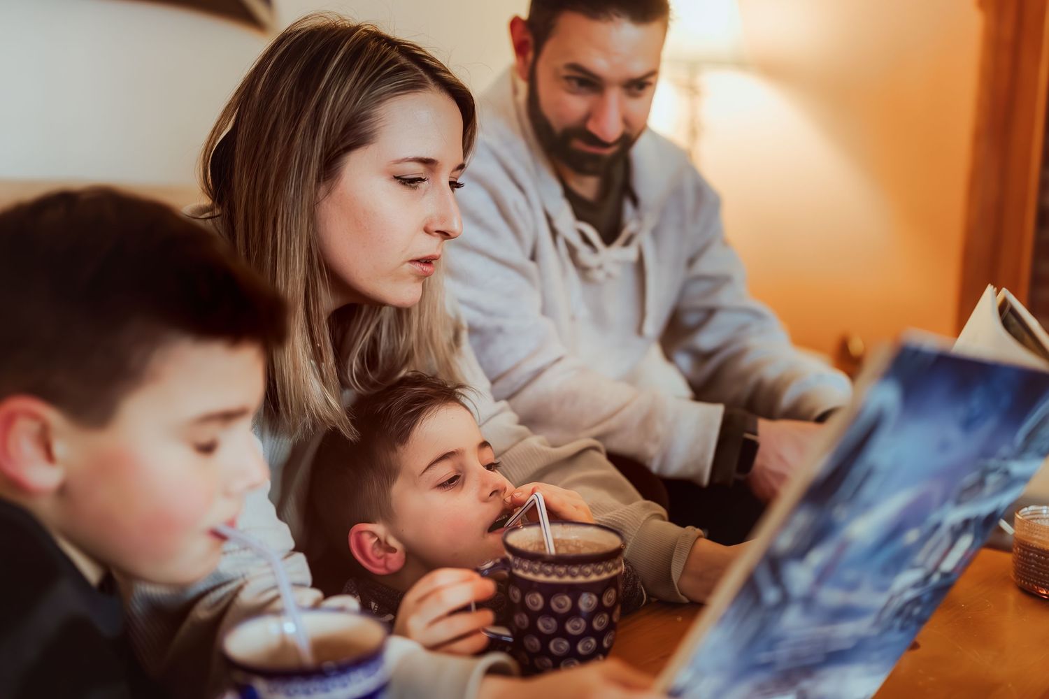 Family gathered together on couch reading bedtime story with hot cocoa on cozy evening at home.