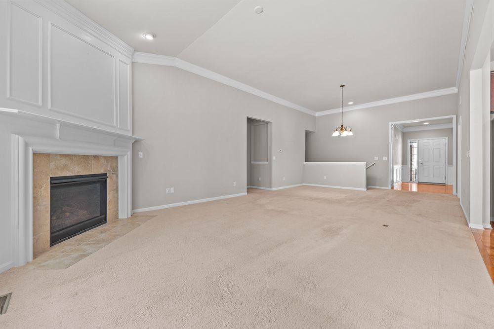 Spacious living room with vaulted ceilings, white fireplace with tile surround, and neutral carpet flooring.