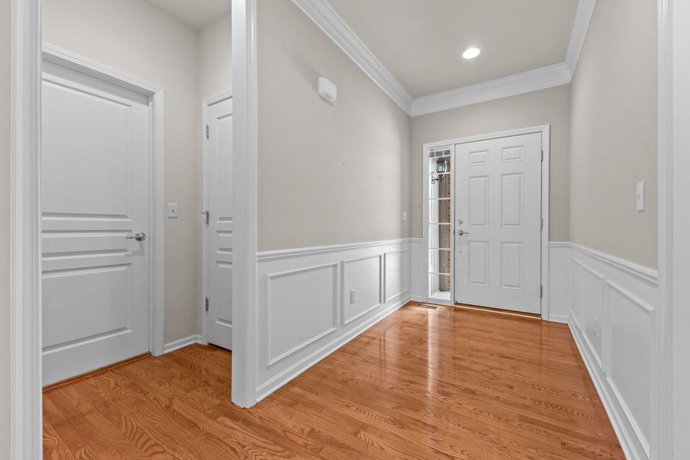 Bright foyer with hardwood floors, wainscoting, crown molding, recessed lighting, and white paneled doors.