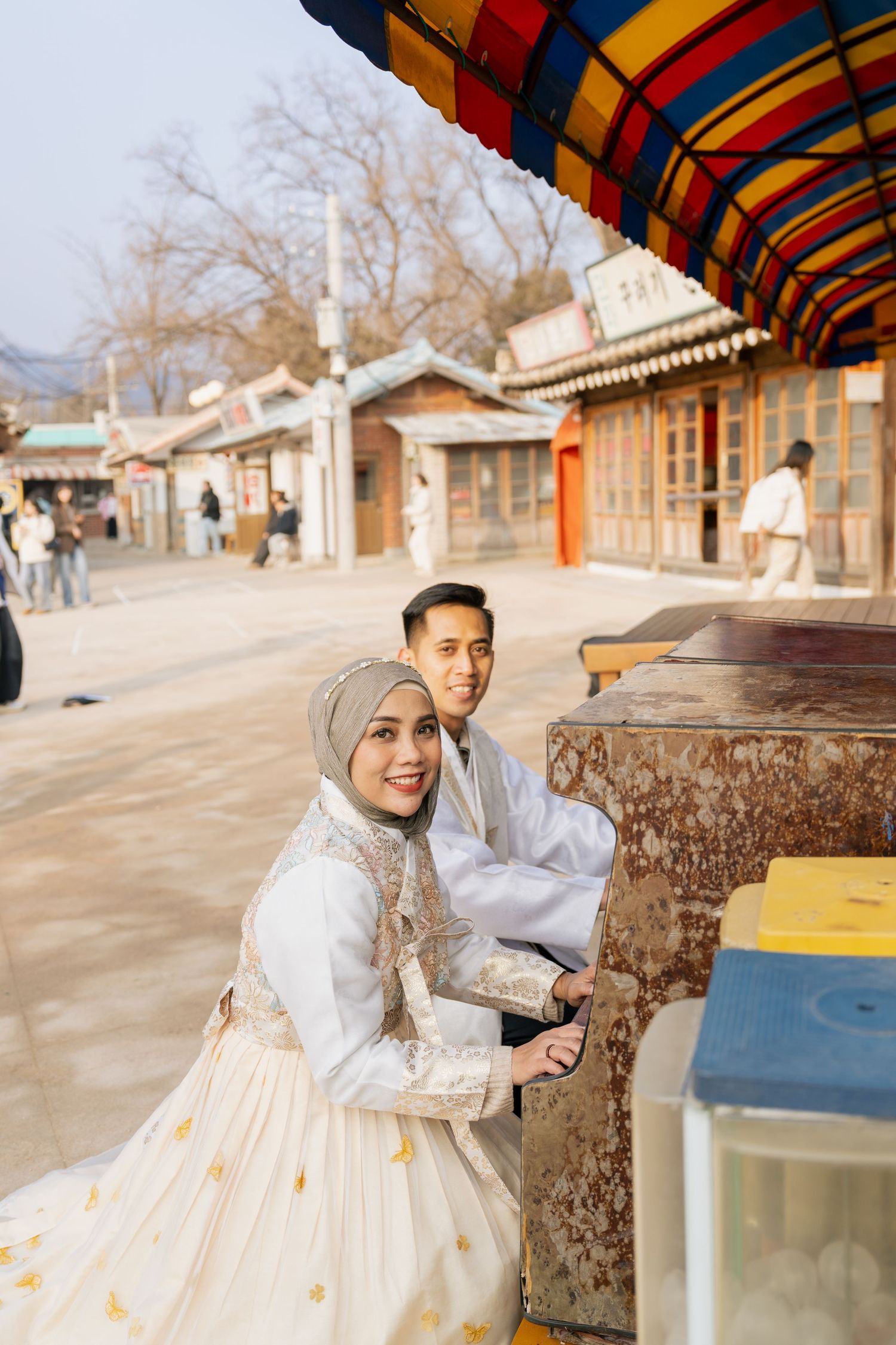A series of candid moments captured at a traditional Korean folk village with colorful striped awnings and rustic buildings.