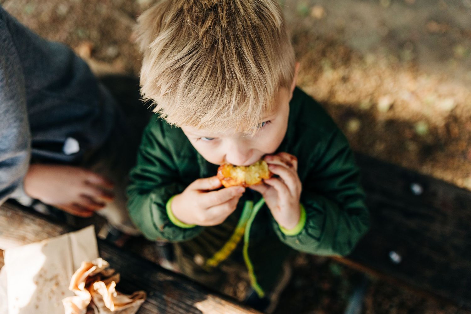 A young child takes a big bite of a freshly baked doughnut outdoors in Charlotte, NC.