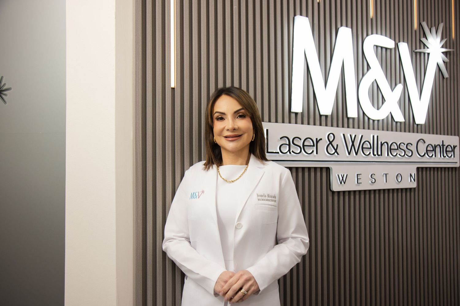 Medical professional in white lab coat stands in front of modern wellness center signage and office decor.