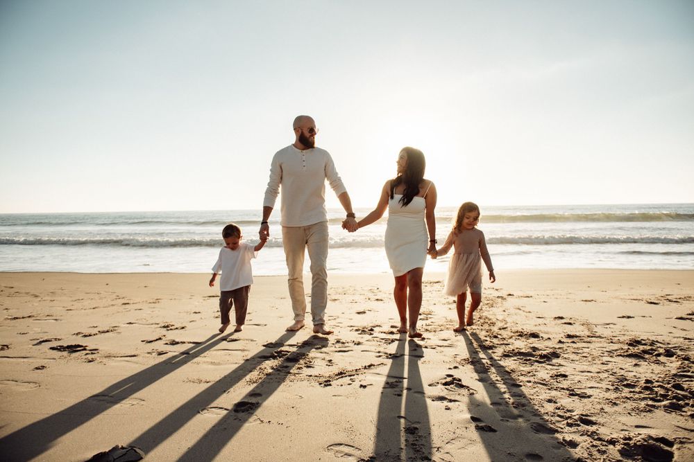 A family walks hand in hand along the beach at sunset casting long shadows.