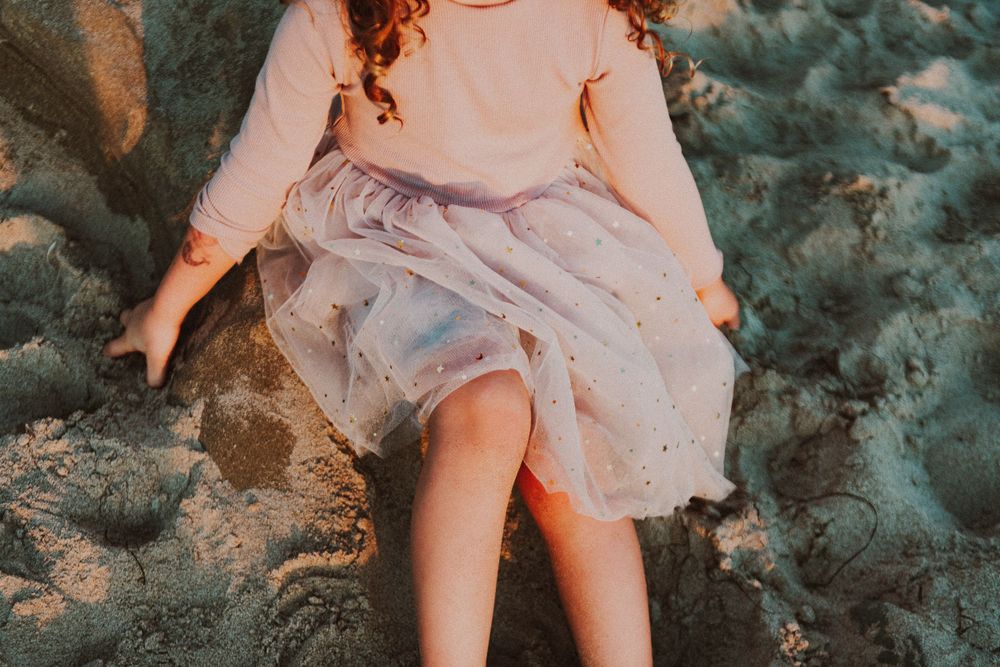 A person in a flowing dress sits on rocky terrain during golden hour.