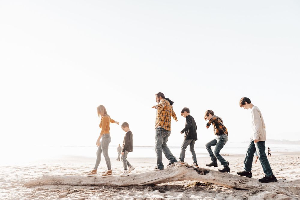 A line of people walking and jumping together on a sandy beach during a bright day.