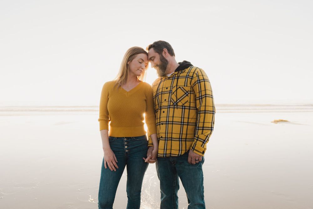 Couple in casual attire standing close together on a misty beach.