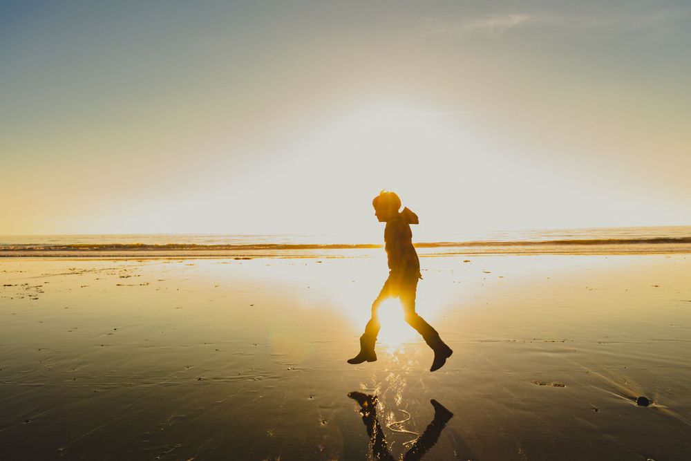 Silhouette of person walking on reflective wet sand during golden hour sunset.