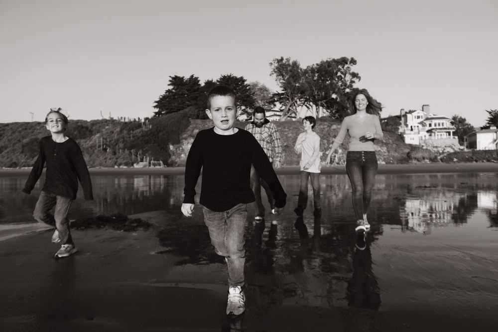 Black and white photo of people walking along a waterfront path with reflections.