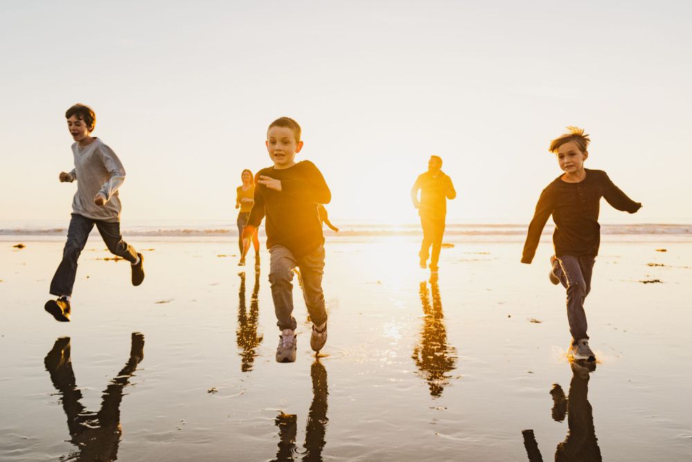 Children running and playing on wet sand beach during sunset with reflections.