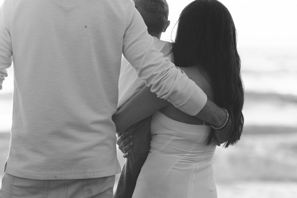 A couple embraces while standing on the beach in black and white.