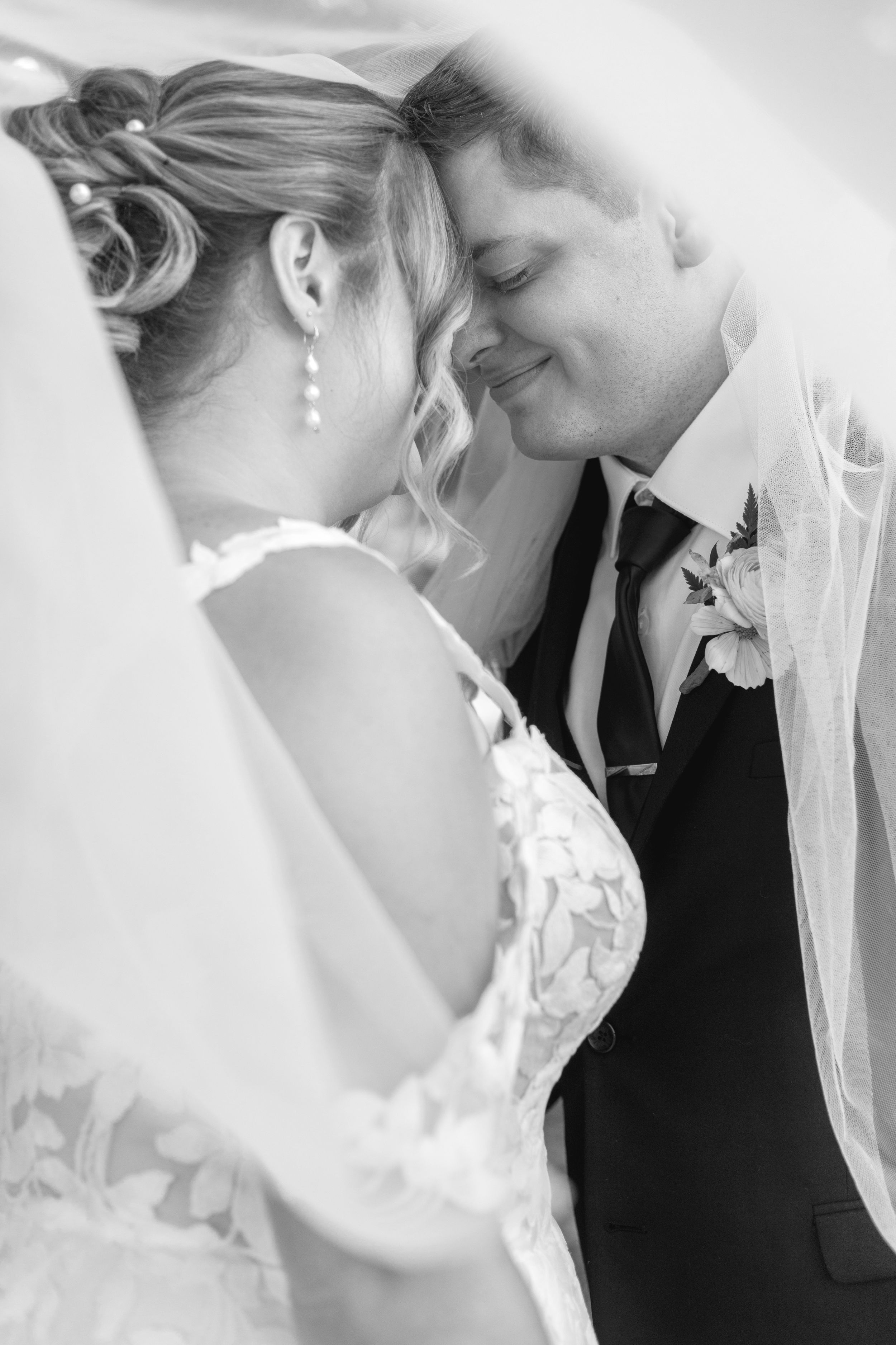 A romantic black and white wedding portrait showing a tender moment between newlyweds under a veil.