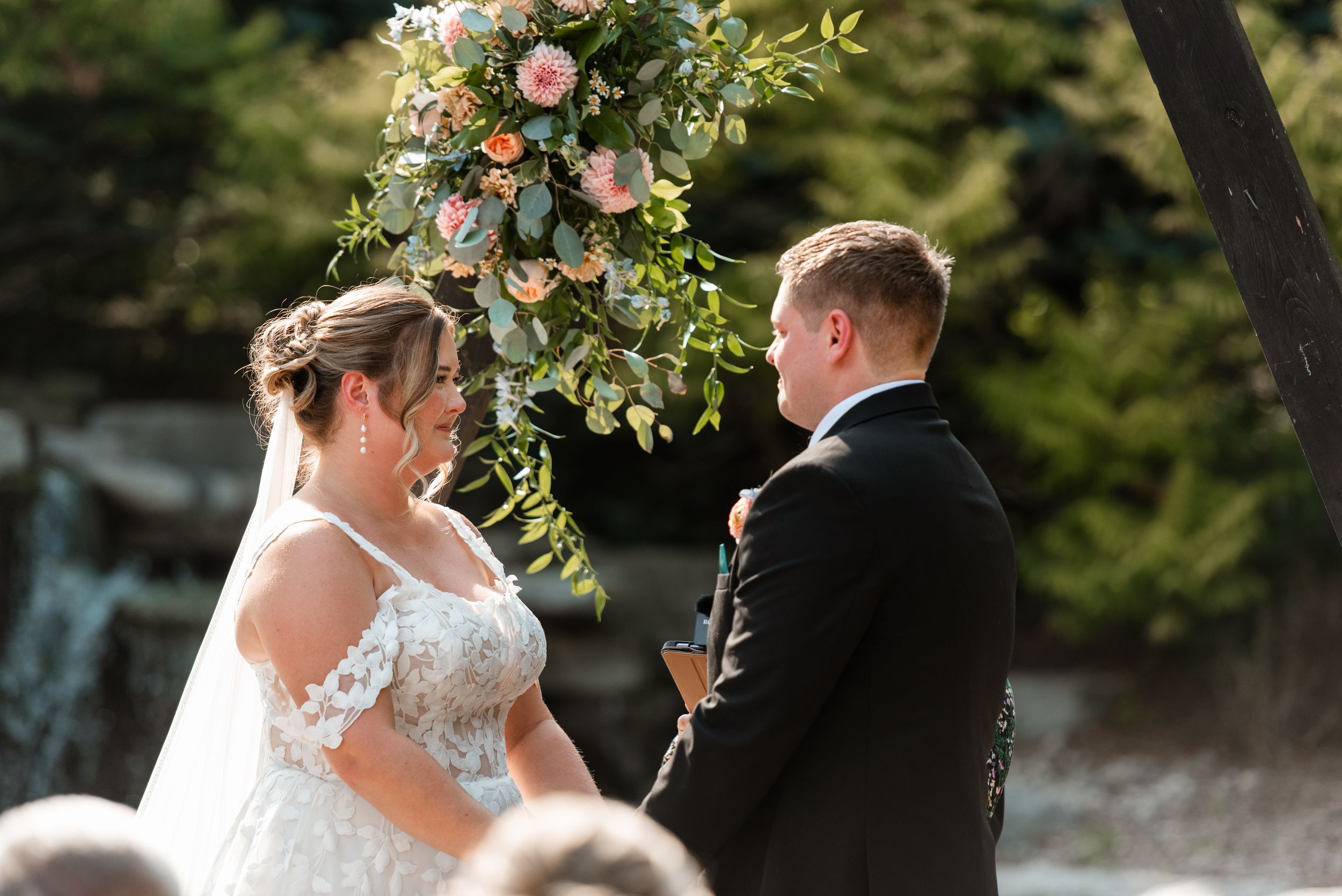 A bride and groom share intimate moments during their outdoor wedding ceremony surrounded by lush greenery.