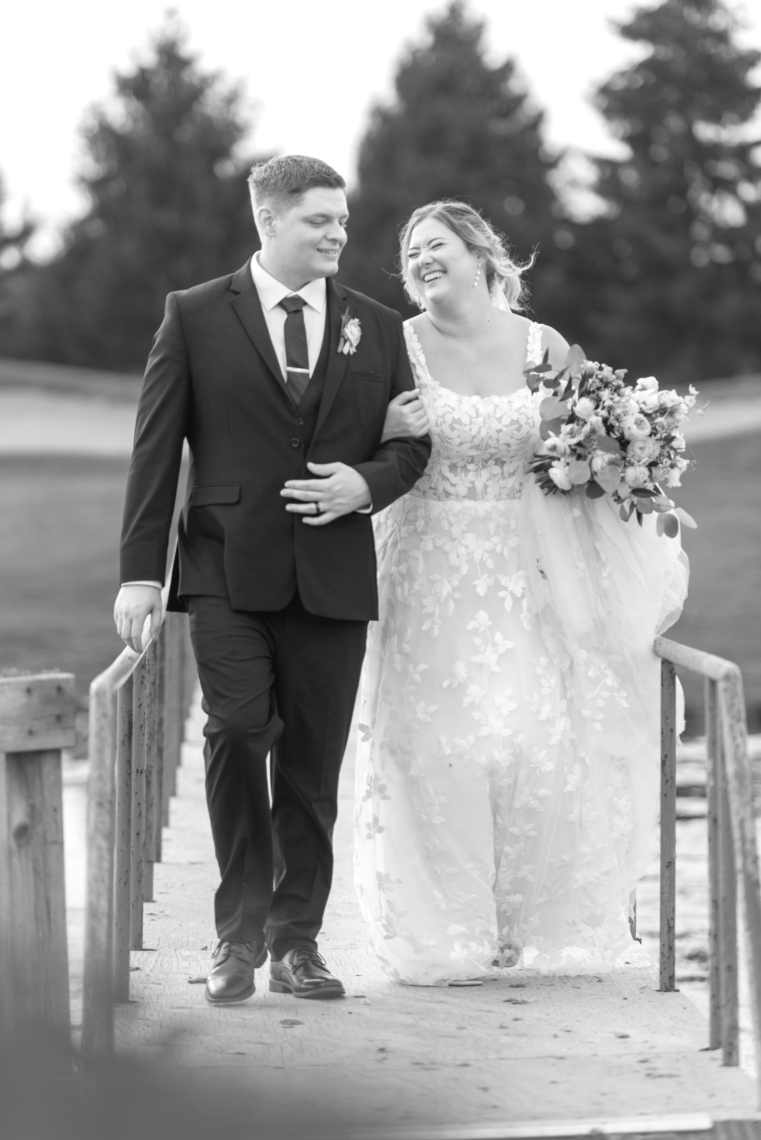 Wedding couple sitting together on wooden dock during outdoor ceremony at sunset.