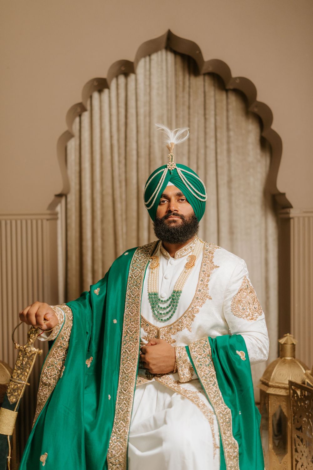 Traditional Indian groom wearing an elegant emerald green sherwani with gold embroidery and matching turban poses for portraits.