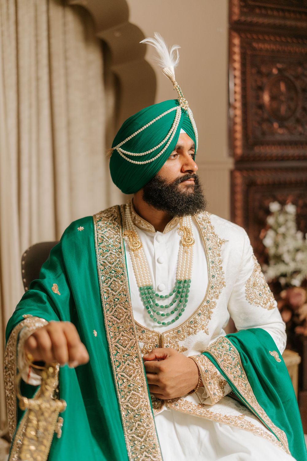 Traditional Sikh groom wearing emerald green turban and sherwani with gold embroidery and layered pearl necklaces.