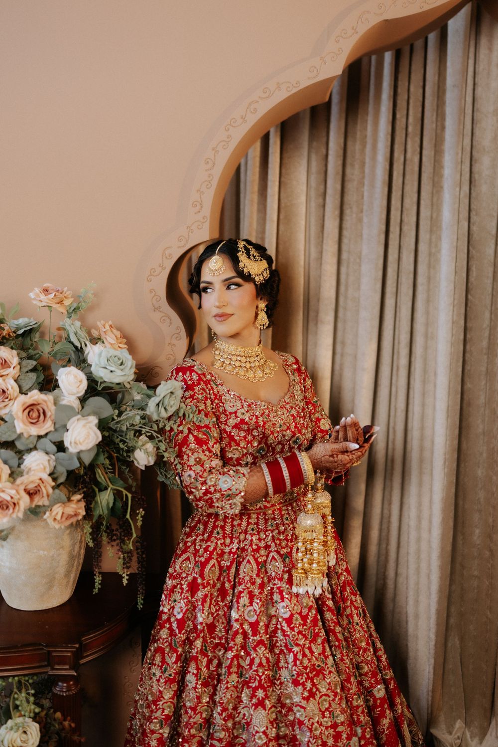 Beautiful red floral dress with delicate embroidery displayed near floral arrangements and curtains.