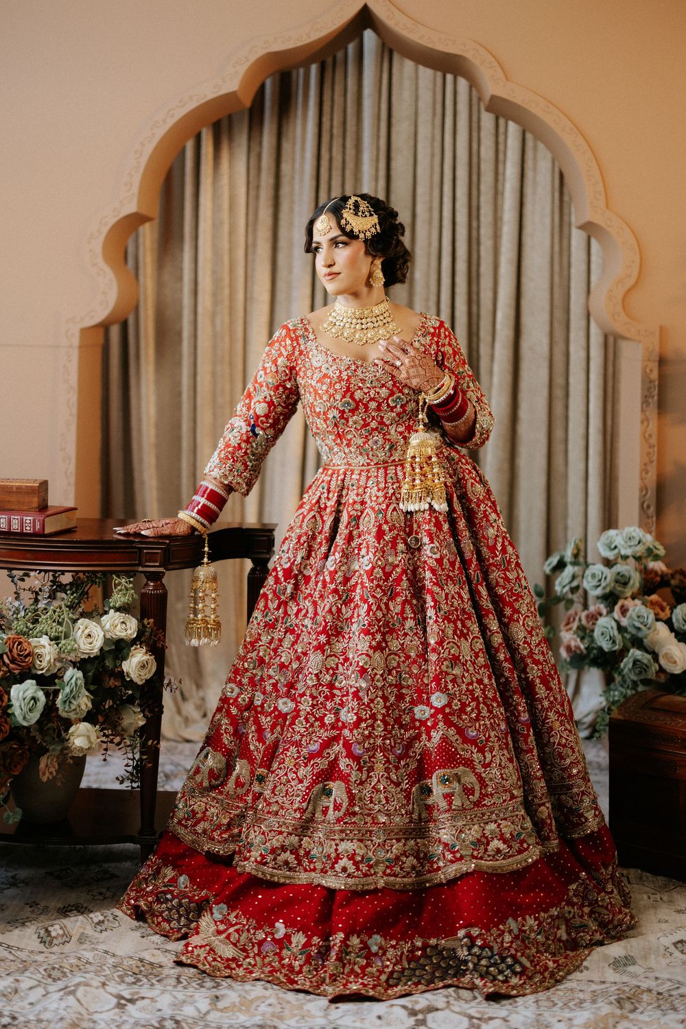 Ornate red and gold bridal lehenga with intricate embroidery displayed in different poses against an elegant backdrop.