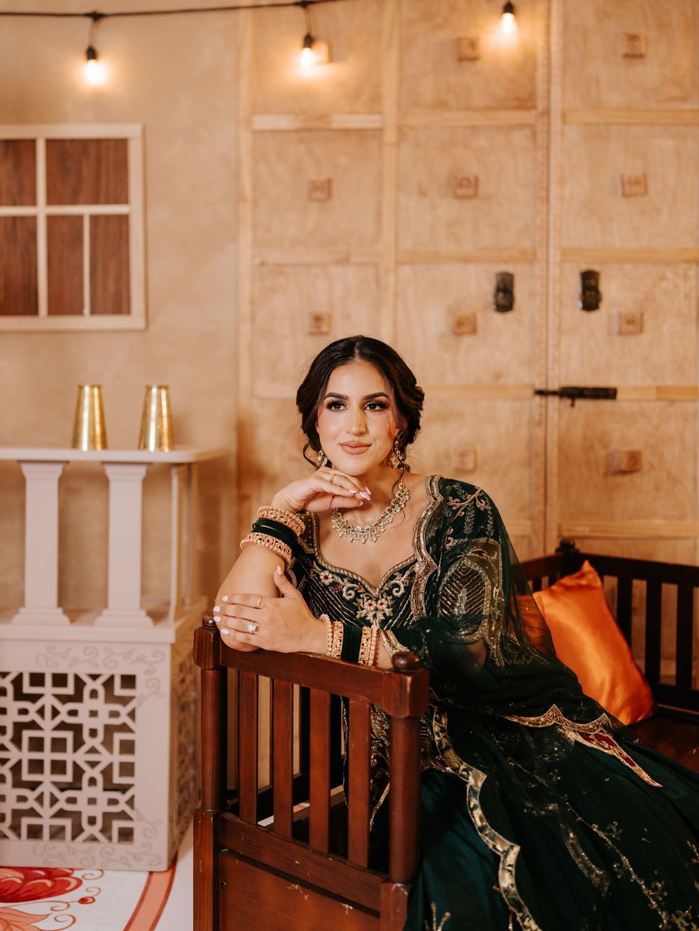 Formal portrait in dark embellished dress with intricate jewelry against beige wall with decorative elements.
