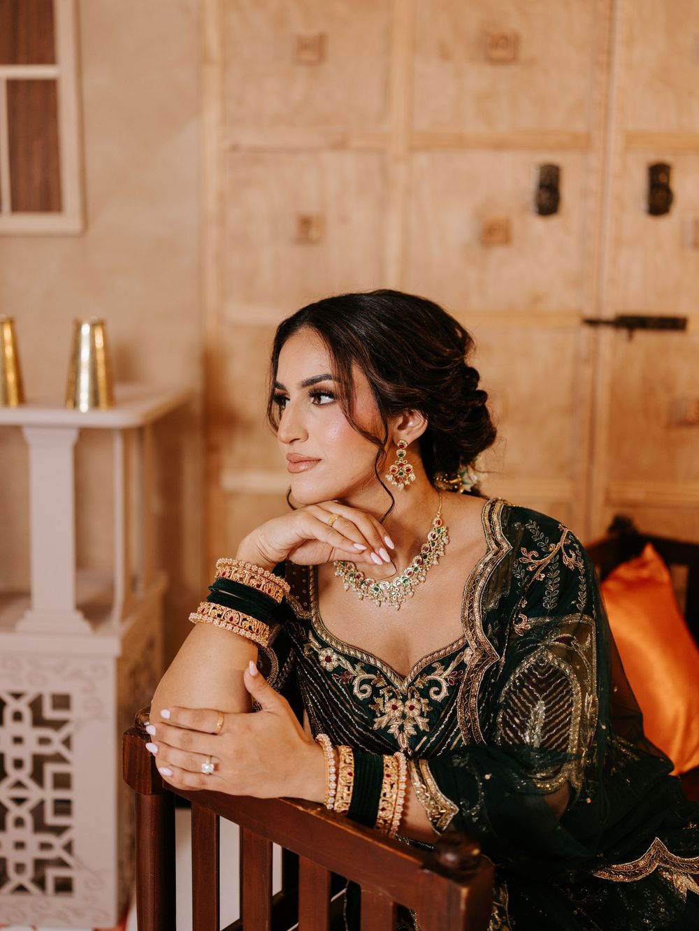 Elegant traditional attire with black and gold embroidered details, ornate jewelry, and upswept hairstyle in warm interior setting.