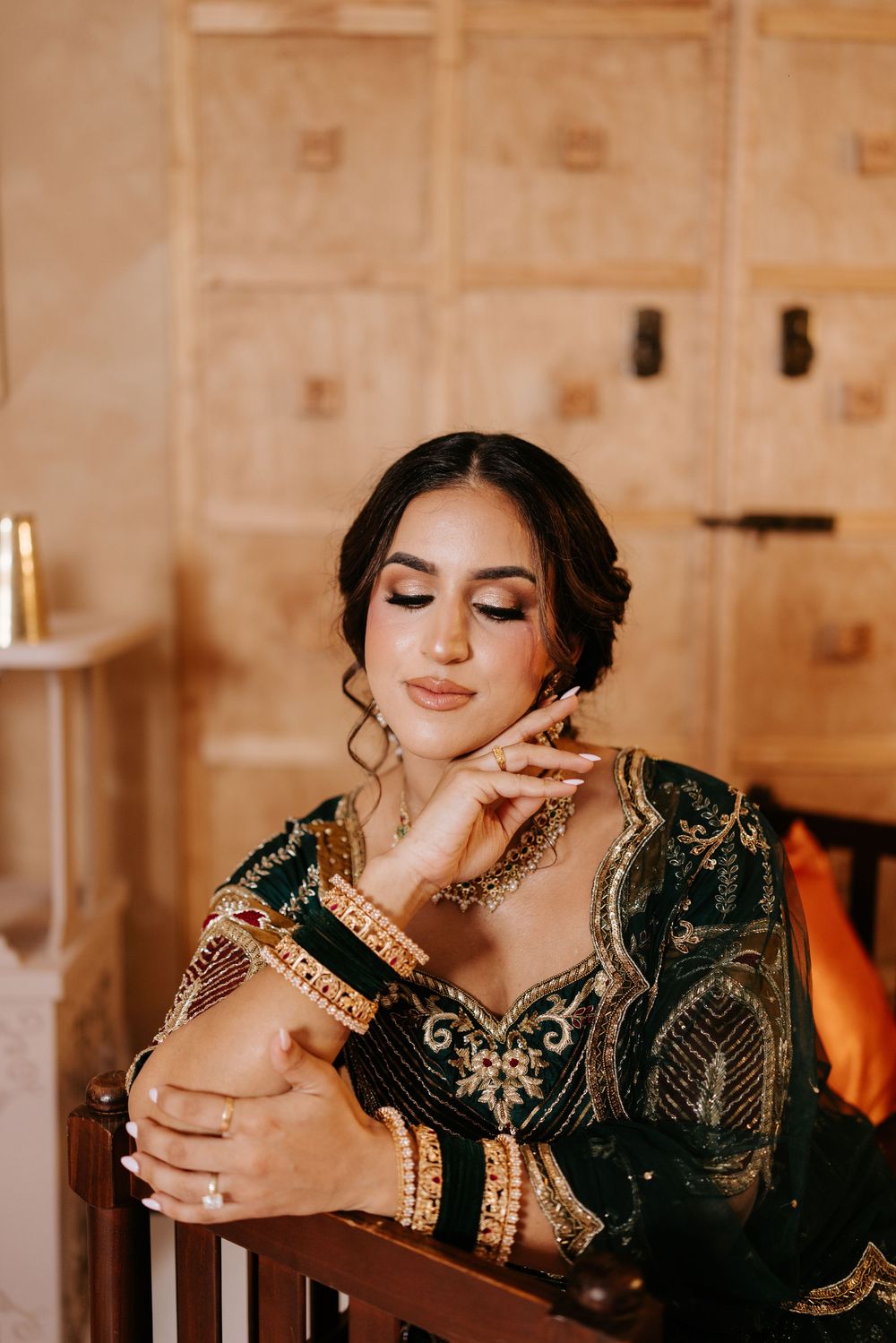 Person wearing an elegant black and gold embroidered dress poses with a glass in a warm-lit wooden interior setting.