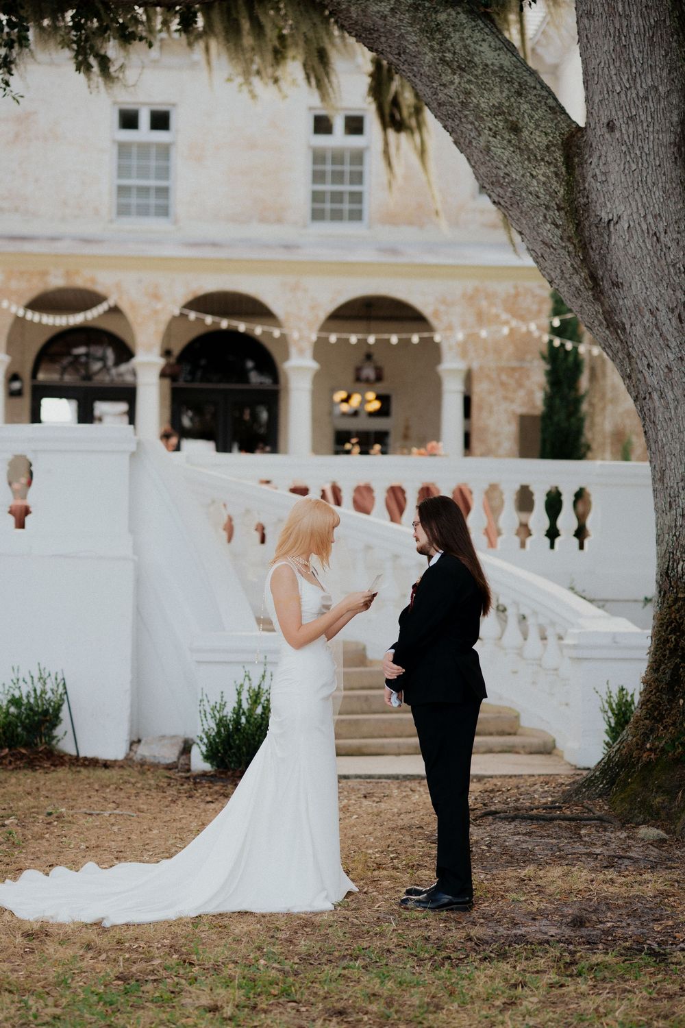 A wedding couple shares a first look moment in an outdoor garden setting with historic architecture.