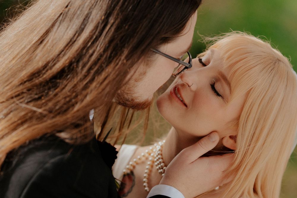 A romantic couple shares tender kisses in a garden setting with soft natural lighting and greenery in the background.