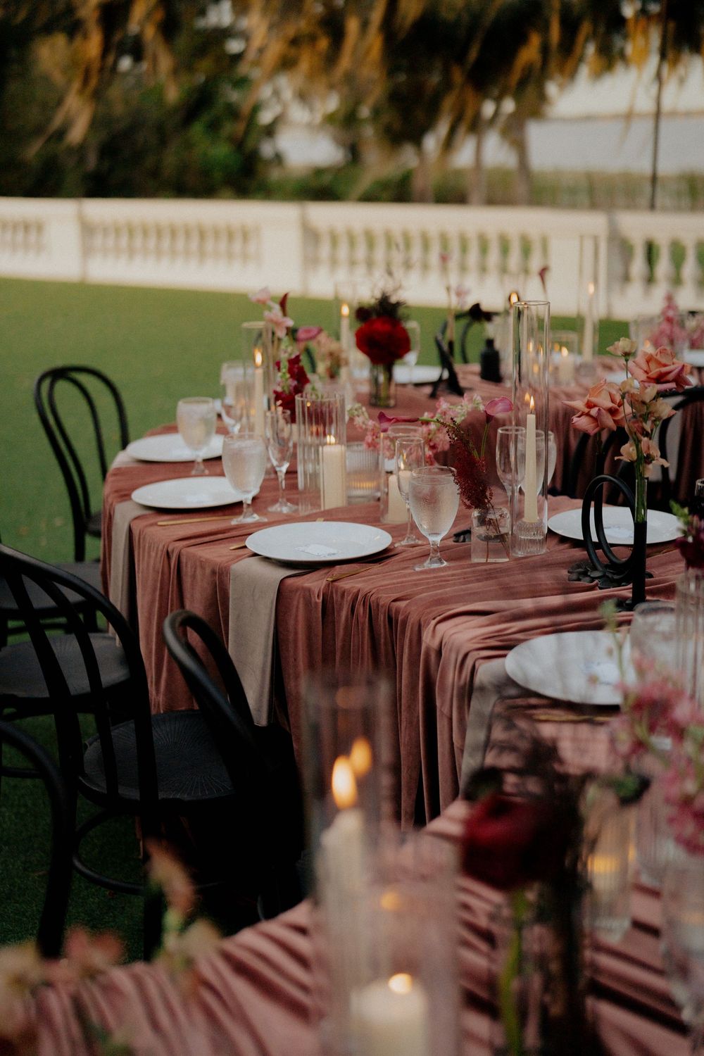 Elegant outdoor wedding reception tables set with dusty rose linens and black chairs at sunset.