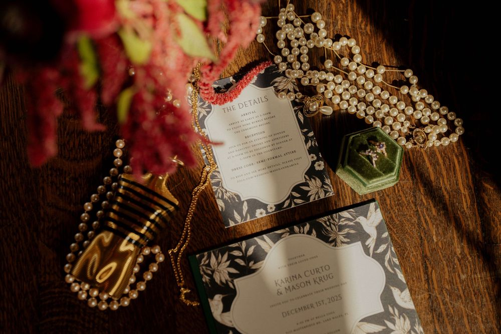 Wedding invitation suite with gold jewelry and floral details arranged on rustic wooden surface.