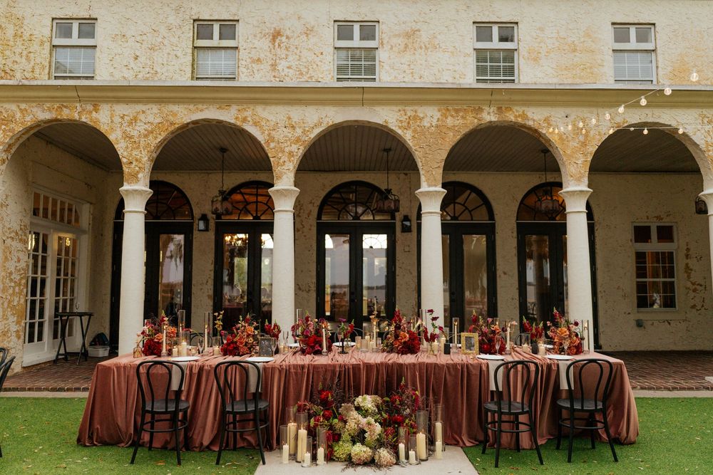 Tables and chairs set up for an elegant outdoor wedding reception under stone archways and columns.