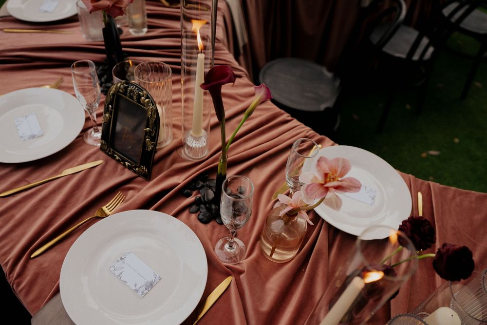 Place settings with white plates and wine glasses on tables covered in dusty rose colored linens.