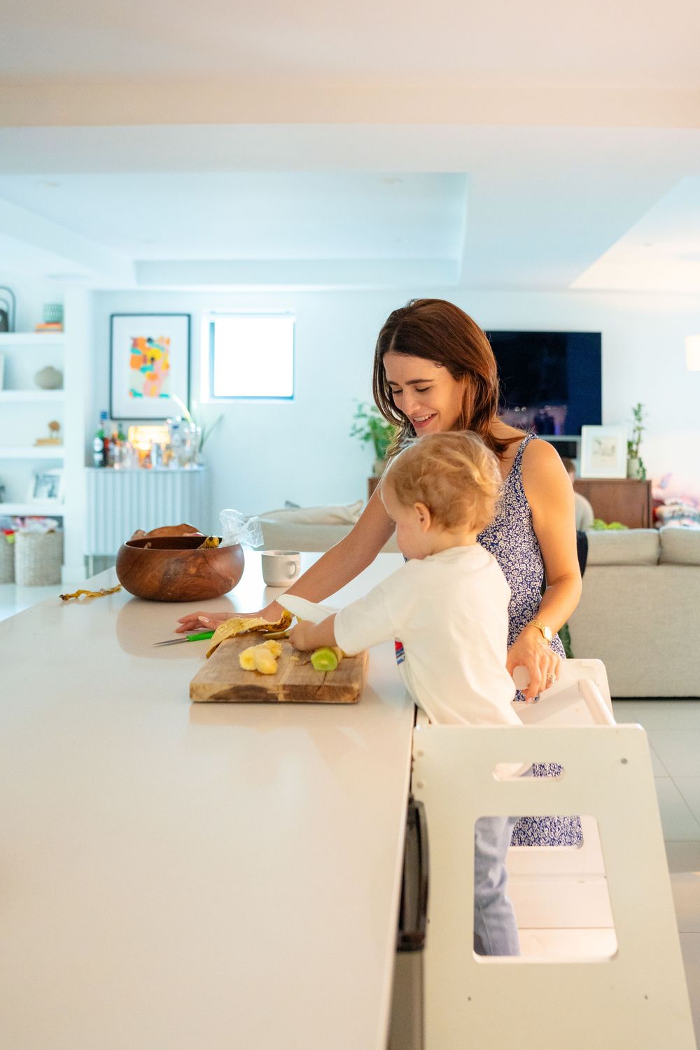 A parent and child prepare food together at a white kitchen counter in a modern, bright home.