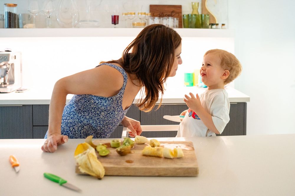 Parent and child bonding while cooking together at kitchen counter with wooden cutting board.