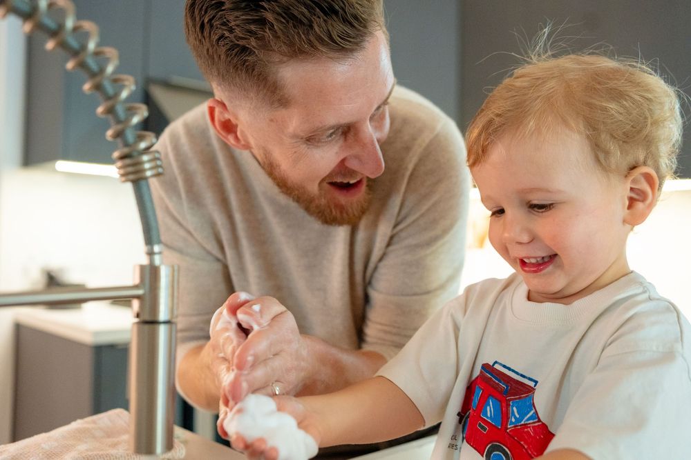 Two people washing hands together at a kitchen sink with a modern faucet.