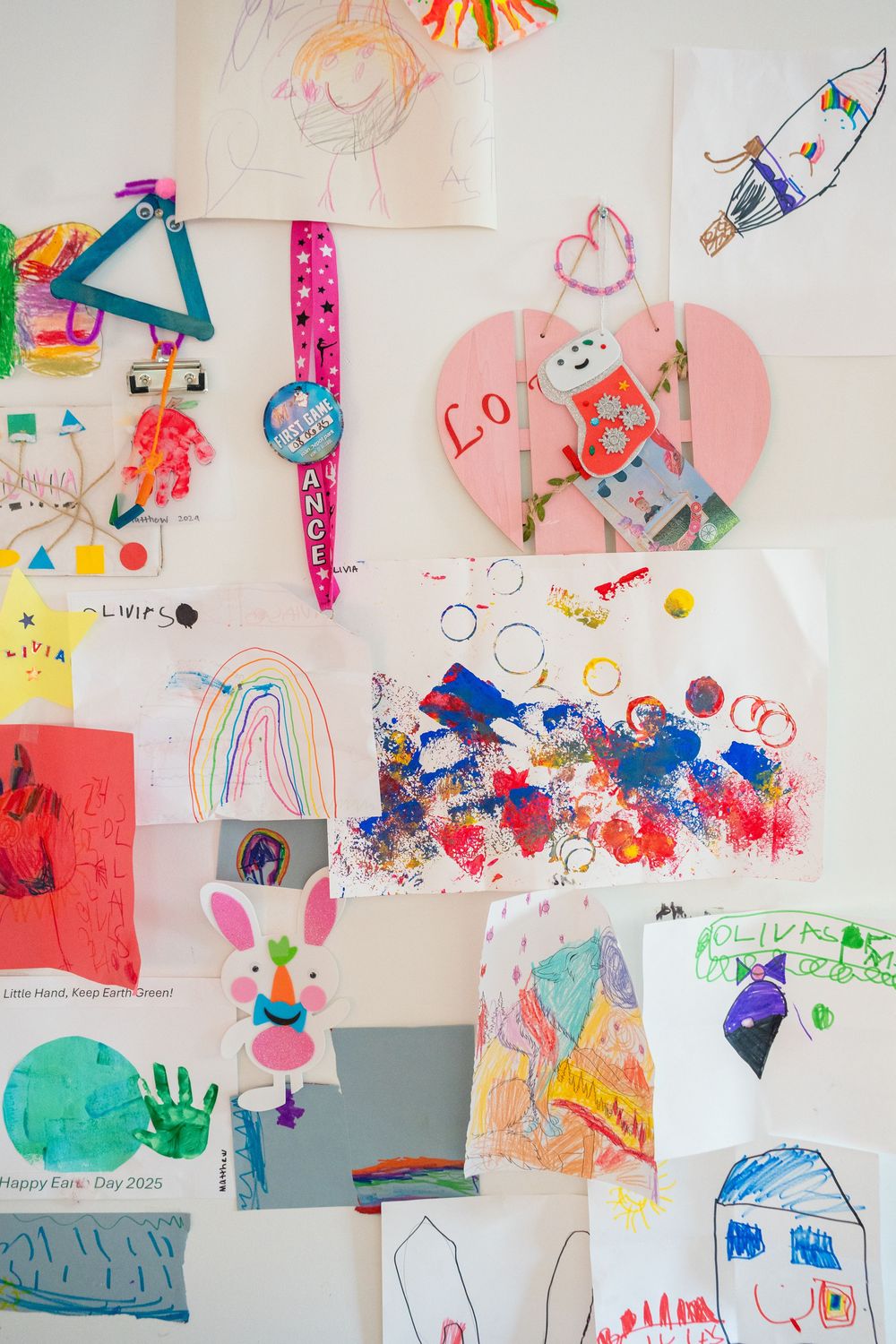 Colorful children's artwork and drawings displayed on wall featuring hearts, bunnies and abstract designs.