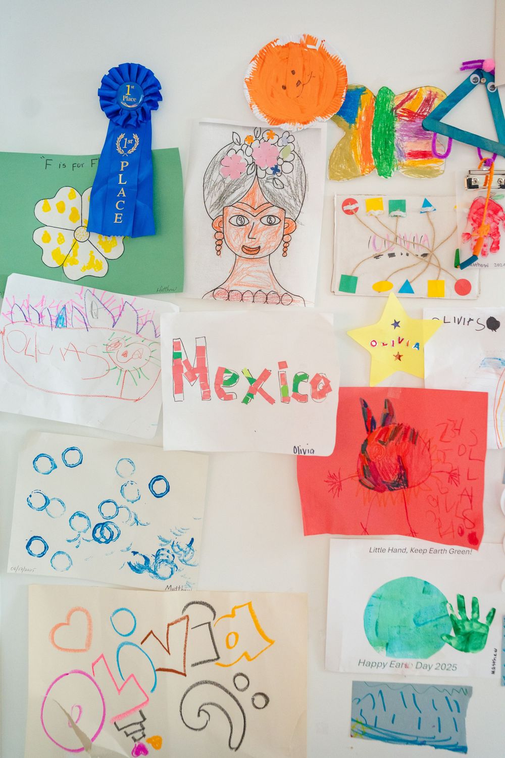 Children's artwork and colorful drawings displayed on a white wall featuring various shapes, figures, and the word Mexico.