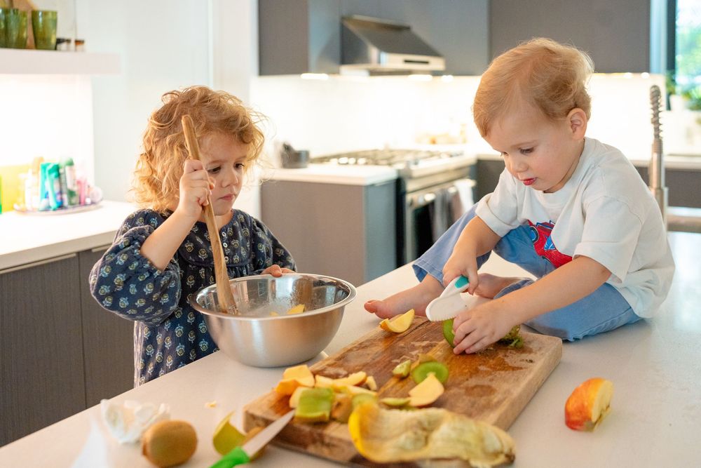 Parents and child working together to slice fresh fruits and vegetables in a contemporary kitchen.